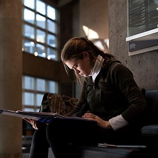 在TCU Moudy Hall North的阳光明媚的大厅里，一位年轻女子独自坐在那里专心地看着她的书.